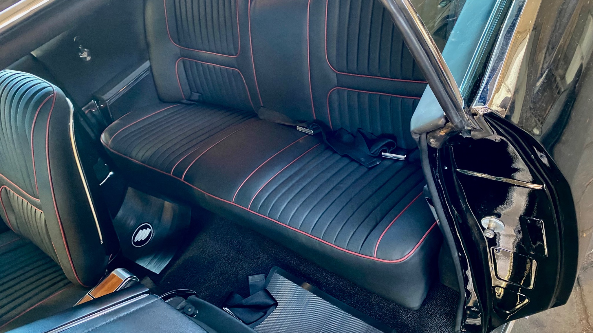 Wnętrze odrestaurowanego klasycznego samochodu Buick z czarną tapicerką i czerwonymi przeszyciami, widoczny fragment drzwi i dywanik z logo Buick.