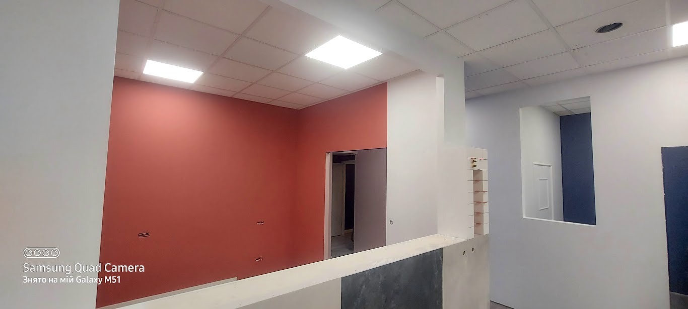 Wnętrze po malowaniu: ściana w odcieniach terakoty kontrastuje z bielą, widoczne otwory na gniazdka, sufit kasetonowy z lampami. Widok na sąsiednie pomieszczenia.