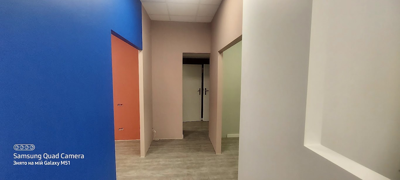 Wnętrze po malowaniu: ściany w odcieniach błękitu, różu i bieli, widoczne drzwi w głębi. Minimalistyczny design, świeżo pomalowane powierzchnie, brak dekoracji.