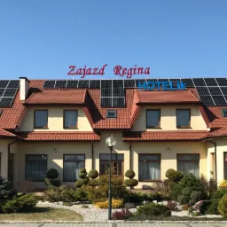 Budynek Zajazdu Regina z panelami słonecznymi na dachu, widoczny napis HOTELIK, otoczenie z zadbaną roślinnością.