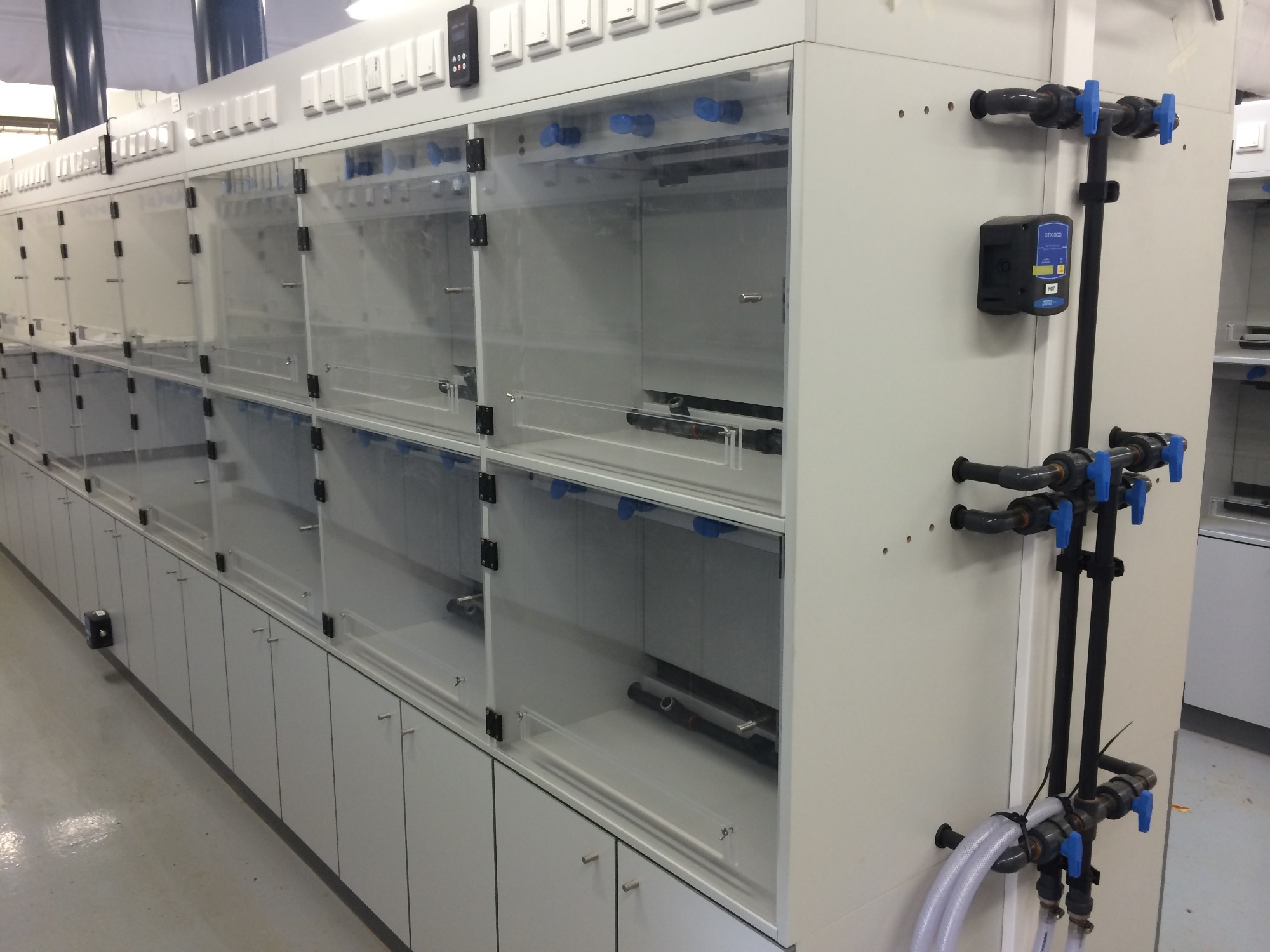 Rząd przezroczystych komór z instalacją wodną i zaworami, prawdopodobnie w laboratorium lub innym środowisku przemysłowym.