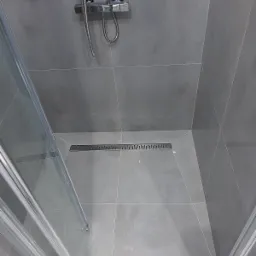 Nowoczesna kabina prysznicowa z szarymi płytkami, widoczny odpływ liniowy i chromowana bateria.