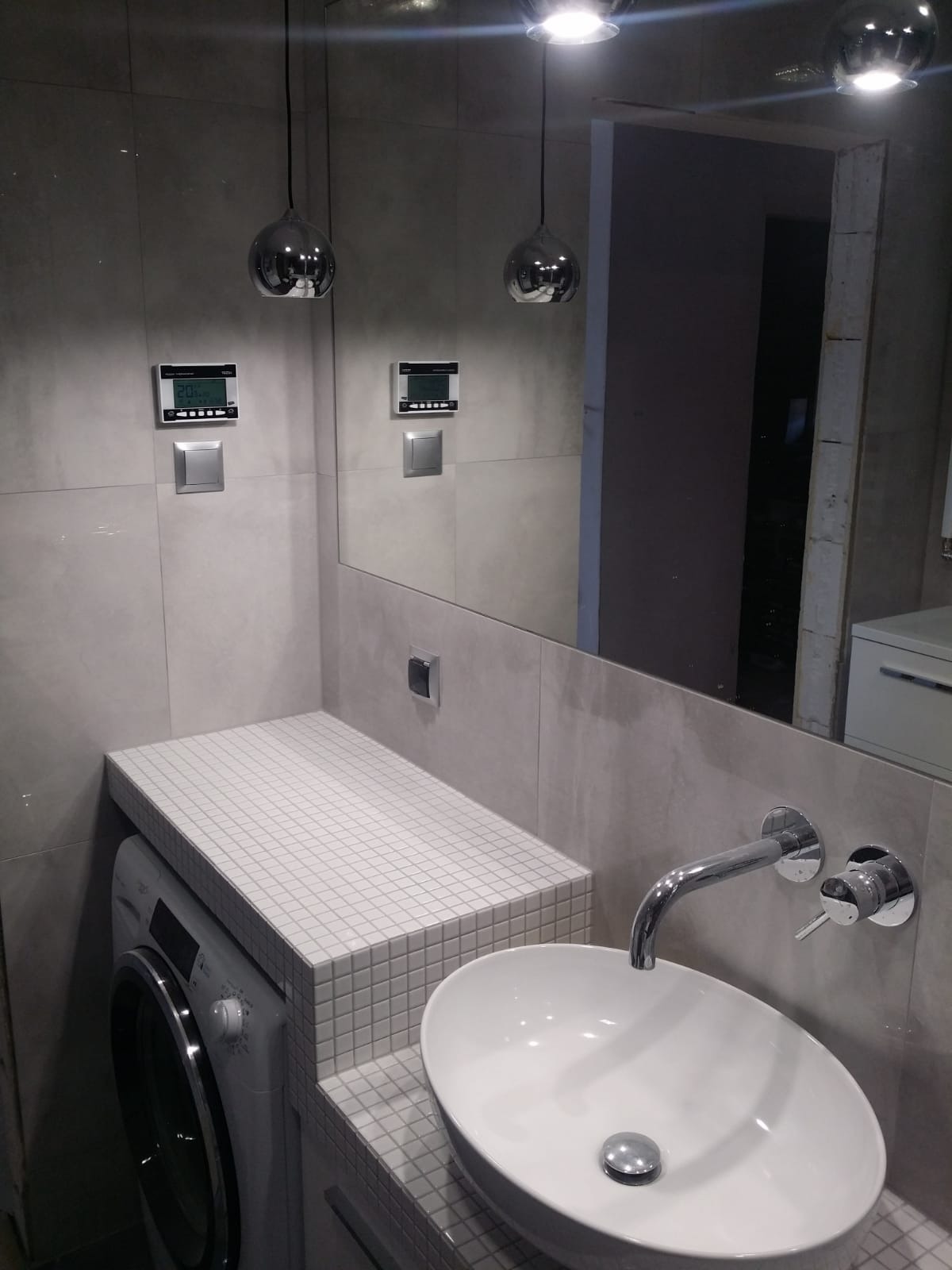 Nowoczesna łazienka z umywalką nablatową, mozaiką na blacie pralki, chromowaną armaturą i oświetleniem punktowym.