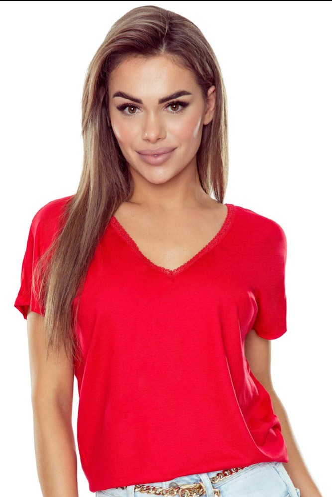 Portret kobiety w czerwonej koszulce z koronkowym dekoltem na białym tle. Widoczny złoty łańcuszek przy spodniach. Uśmiechnięta twarz, profesjonalny makijaż.