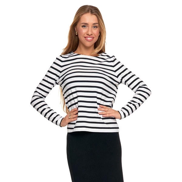 Kobieta prezentuje bluzkę w czarno-białe paski i czarną spódnicę na białym tle. Uśmiechnięta, z rękami na biodrach, patrzy wprost. Prosty, modny strój.