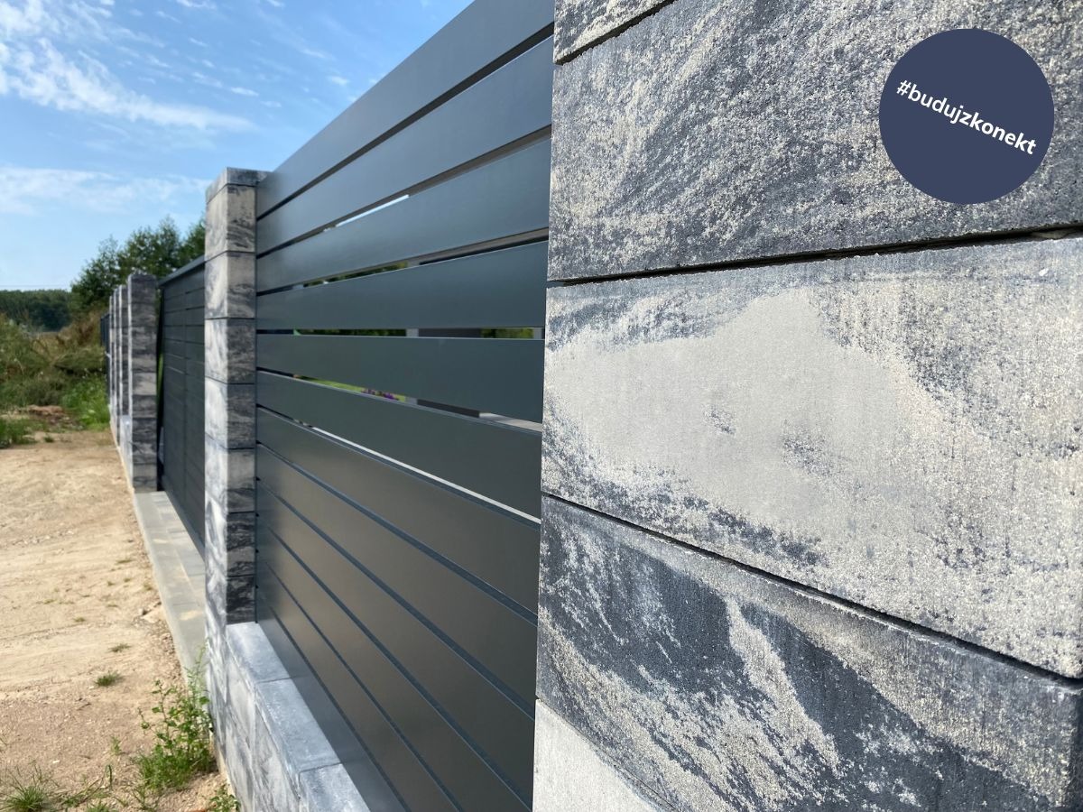 Nowoczesne ogrodzenie panelowe z elementami betonowymi, z widocznym zbliżeniem na fakturę betonowej części i okrągłym logo z hashtagiem w prawym górnym rogu.