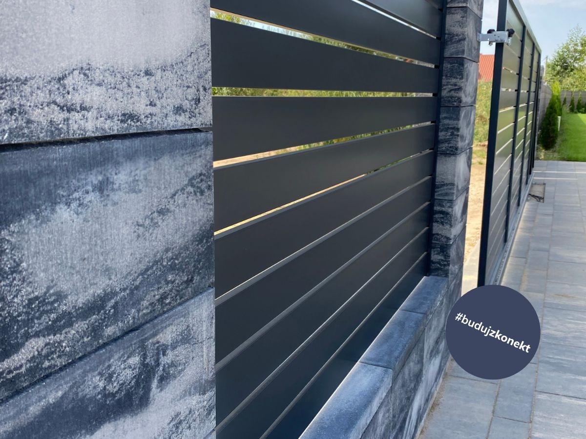 Nowoczesne, poziome przęsła w kolorze grafitowym, zamontowane na słupkach z szarego betonu architektonicznego, tworzące ogrodzenie posesji.