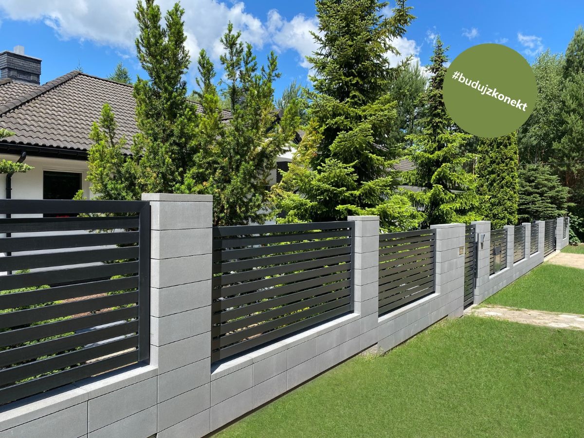 Nowoczesne ogrodzenie z szarych, betonowych słupków i poziomych, czarnych paneli, z zielonym logo #budujzkonekt w prawym górnym rogu, na tle zadbanego trawnika, drzew i domu.