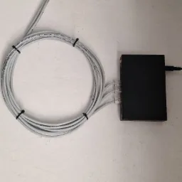 Czarny switch sieciowy z podłączonymi kablami UTP, spiętymi czarnymi opaskami zaciskowymi na tle białej ściany.