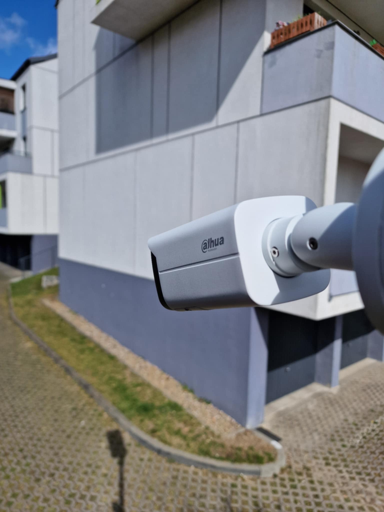 Kamera monitoringu marki Dahua zamontowana na elewacji nowoczesnego budynku mieszkalnego, widok z bliska na obudowę kamery i fragment otoczenia.