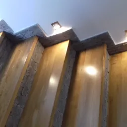 Wykończenie wnętrza w Chyżnem: drewniane panele ścienne z kamiennymi akcentami pod sufitem z oświetleniem punktowym, widok z dołu.