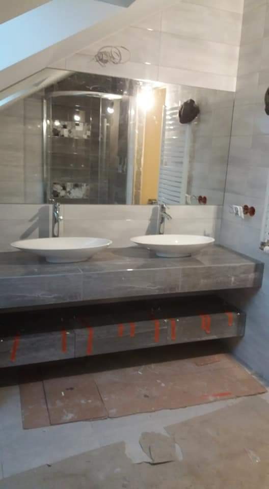 Łazienka w trakcie remontu: dwie białe umywalki na szarym blacie, duże lustro, szare płytki na ścianach, zabezpieczone podłogi.
