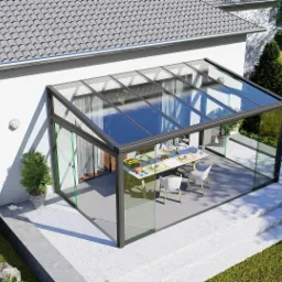 Szklana zabudowa tarasu z czarną ramą, widok z góry. Wewnątrz stół z nakryciem i krzesła. Nowoczesny design, jasne wnętrze, widok na ogród.