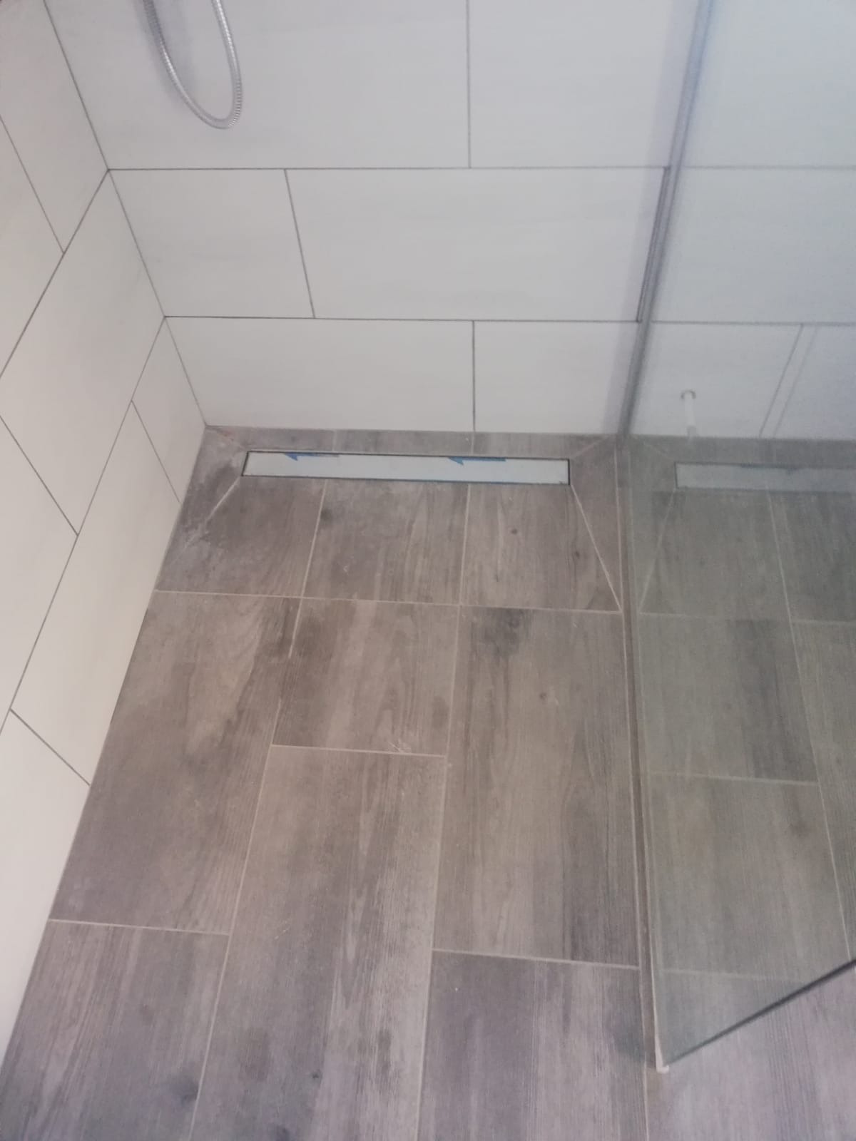 Ukończona kabina prysznicowa w Warszawie z odpływem liniowym, wykończona płytkami imitującymi drewno i białymi płytkami ściennymi.