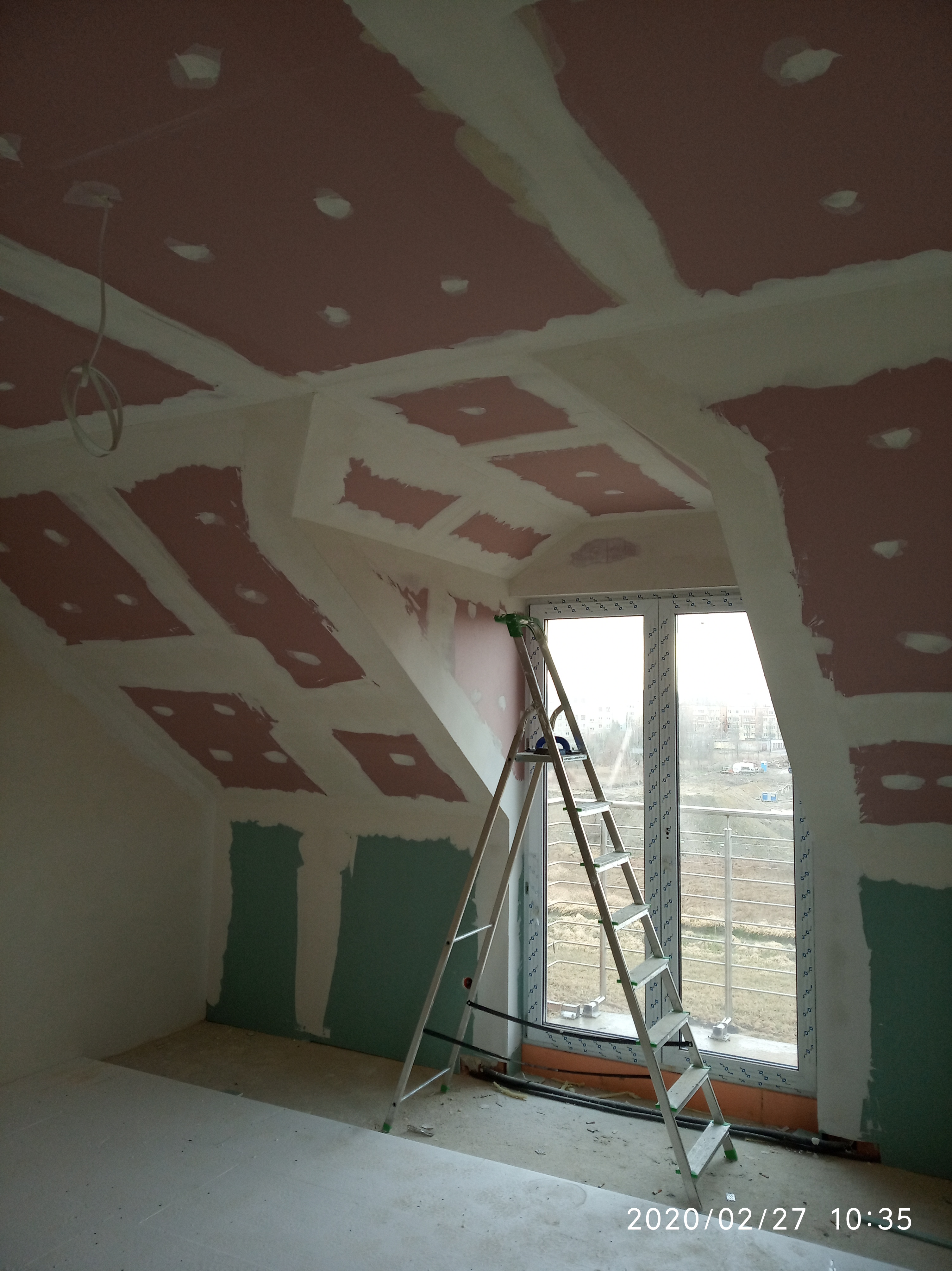 Poddasze w trakcie remontu: widoczne płyty karton gips na skośnym suficie i ścianach, częściowo zaszpachlowane łączenia, drabina aluminiowa oparta o okno, przygotowane otwory pod oświetlenie.