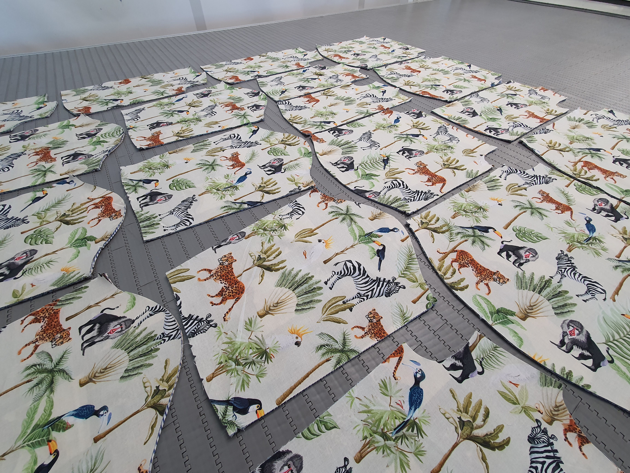 Wykroje odzieżowe z motywem zwierząt tropikalnych, ułożone na szarym podłożu krojowni, widoczne krawędzie z obrysem wykroju.