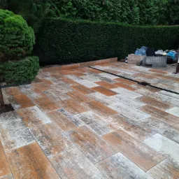 Ułożona nawierzchnia z prostokątnych płyt imitujących drewno, z odpływem liniowym, obok formowany krzew i żywopłot.