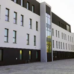 Nowoczesny budynek biurowy z elewacją w kolorach bieli, szarości i czerni, z widocznymi licznymi oknami i brukowanym chodnikiem przed wejściem.