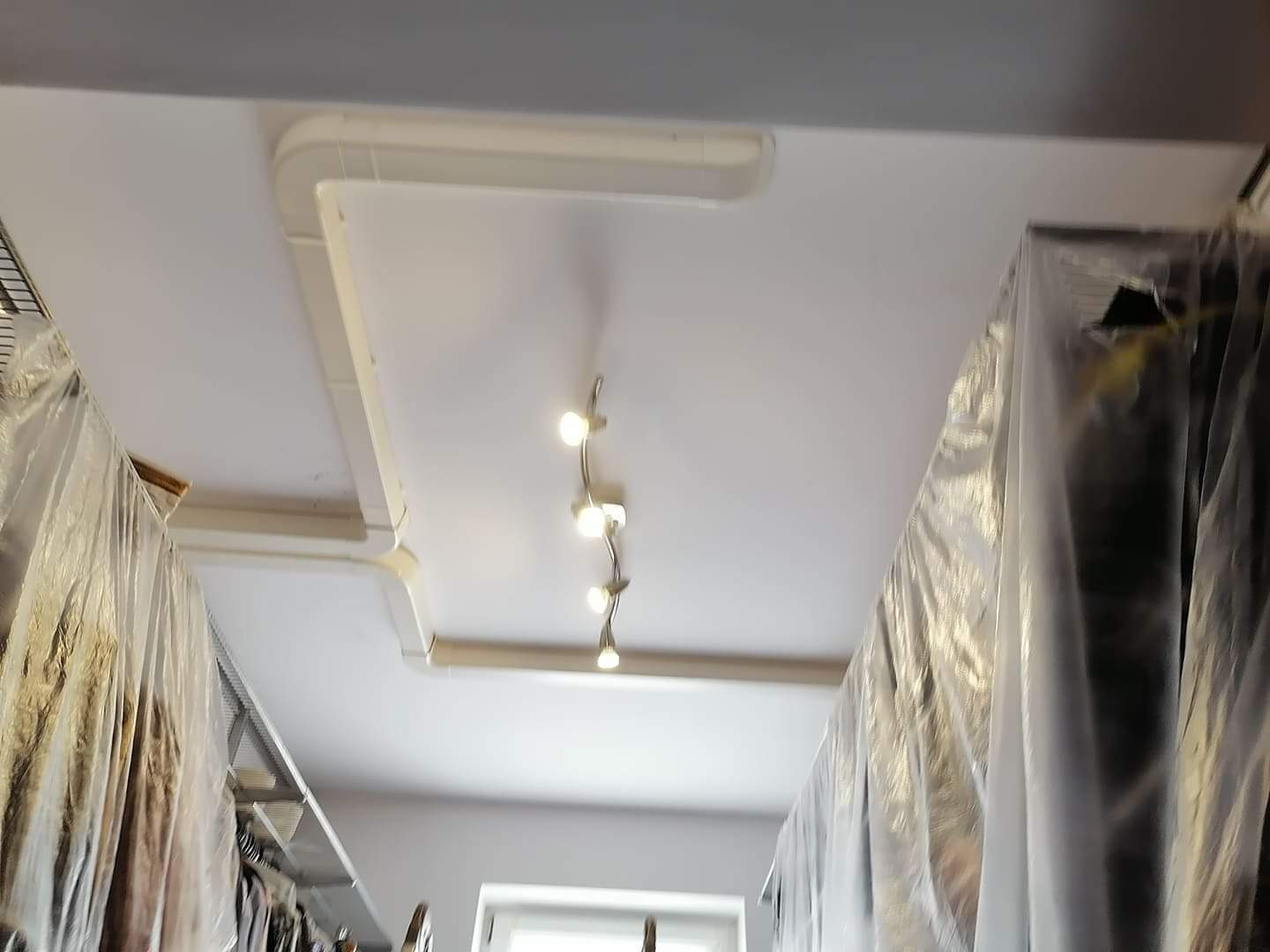 Montaż kanałów wentylacyjnych pod sufitem w pomieszczeniu z zabezpieczonymi folią meblami, widoczne oświetlenie punktowe.