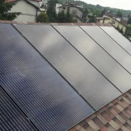 Panele fotowoltaiczne na dachu domu w Tarnowie, widoczne z bliska, z perspektywy dachu. Ciemne panele w kontrastowym ujęciu z jaśniejszymi, odbijającymi światło panelami.