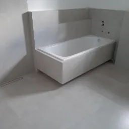 Nowoczesna wanna obudowana płytkami w odcieniach szarości, z widocznym odpływem liniowym w podłodze i elementami instalacji na ścianie.