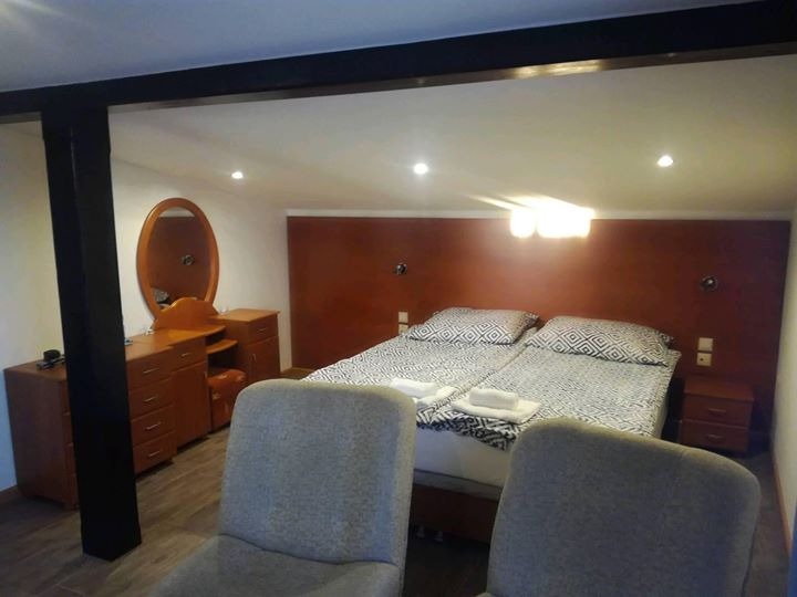 Pokój hotelowy z dwoma pojedynczymi łóżkami z geometryczną pościelą, toaletką z owalnym lustrem i dwoma szarymi krzesłami na pierwszym planie.