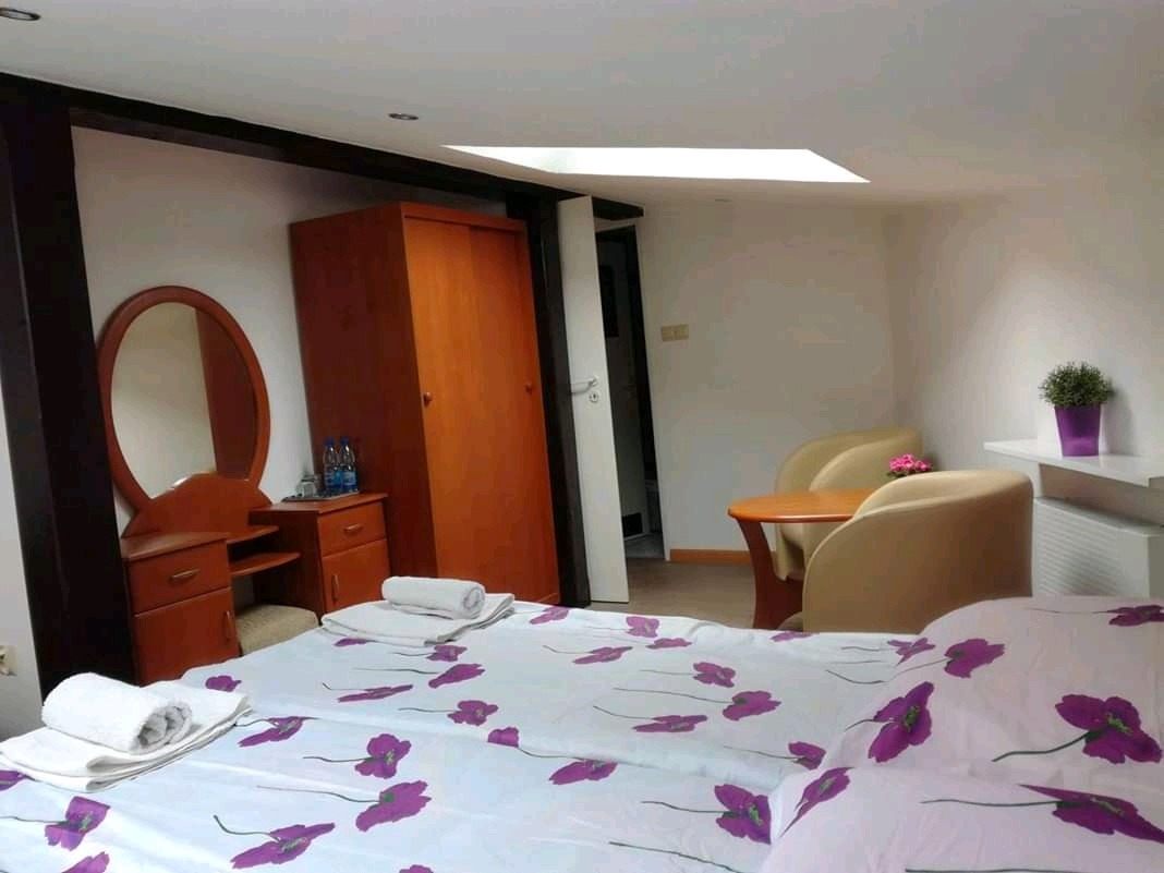 Pokój hotelowy z dwoma łóżkami, toaletką z lustrem, szafą, stolikiem z krzesłami i oknem dachowym.