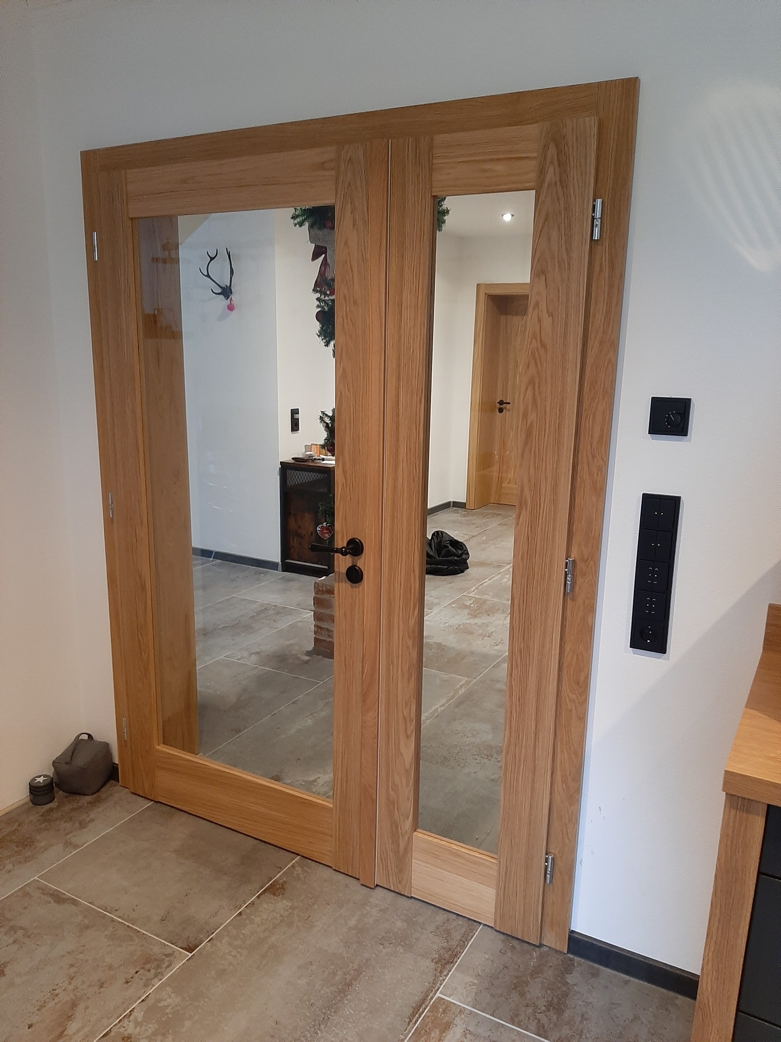 Dwu-skrzydłowe, drewniane drzwi wewnętrzne z przeszkleniami, widok na wnętrze z elementami dekoracyjnymi i podłogą z płytek.