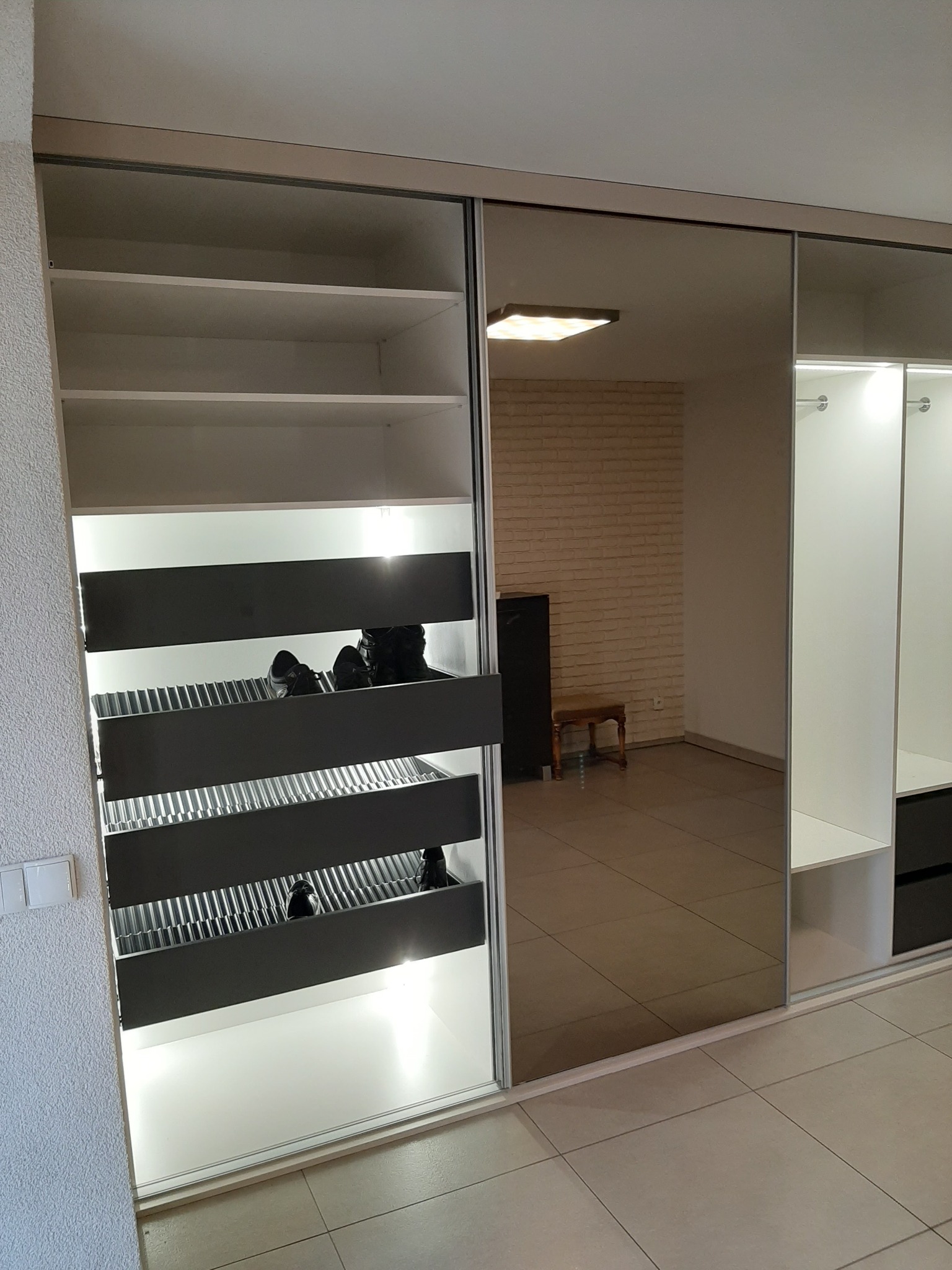 Wnętrze szafy wnękowej z przesuwnymi drzwiami lustrzanymi, widoczne półki, wysuwane kosze na buty i oświetlenie LED.
