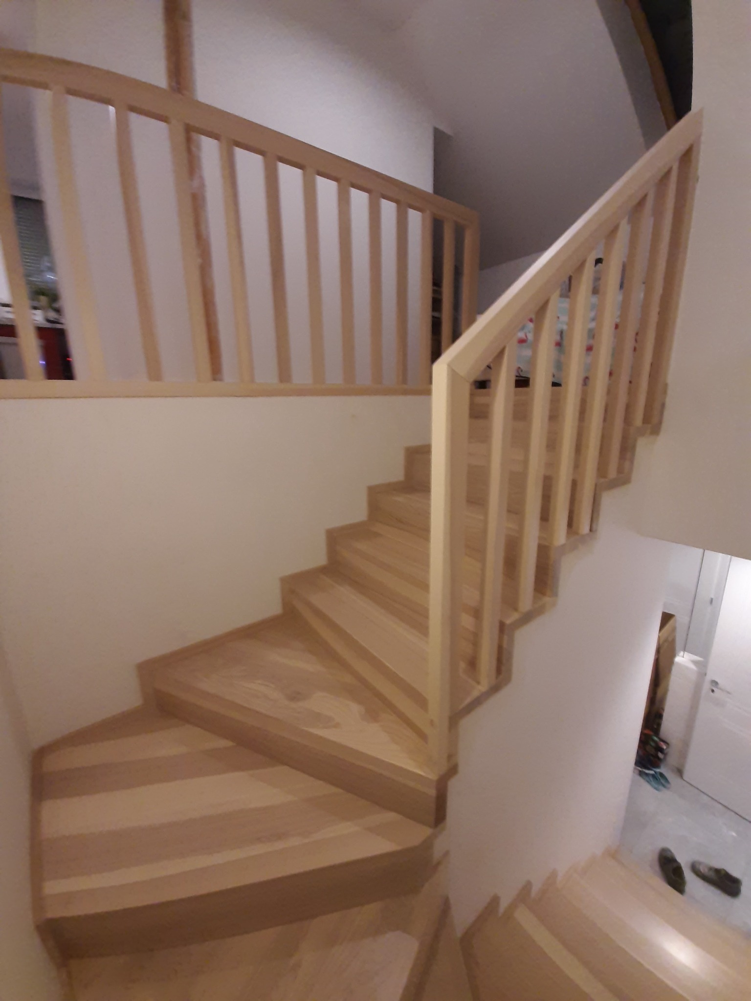 Drewniane schody z jasnego drewna z balustradą, zamontowane w domu w Dziewkowicach, widok z dołu na górę.