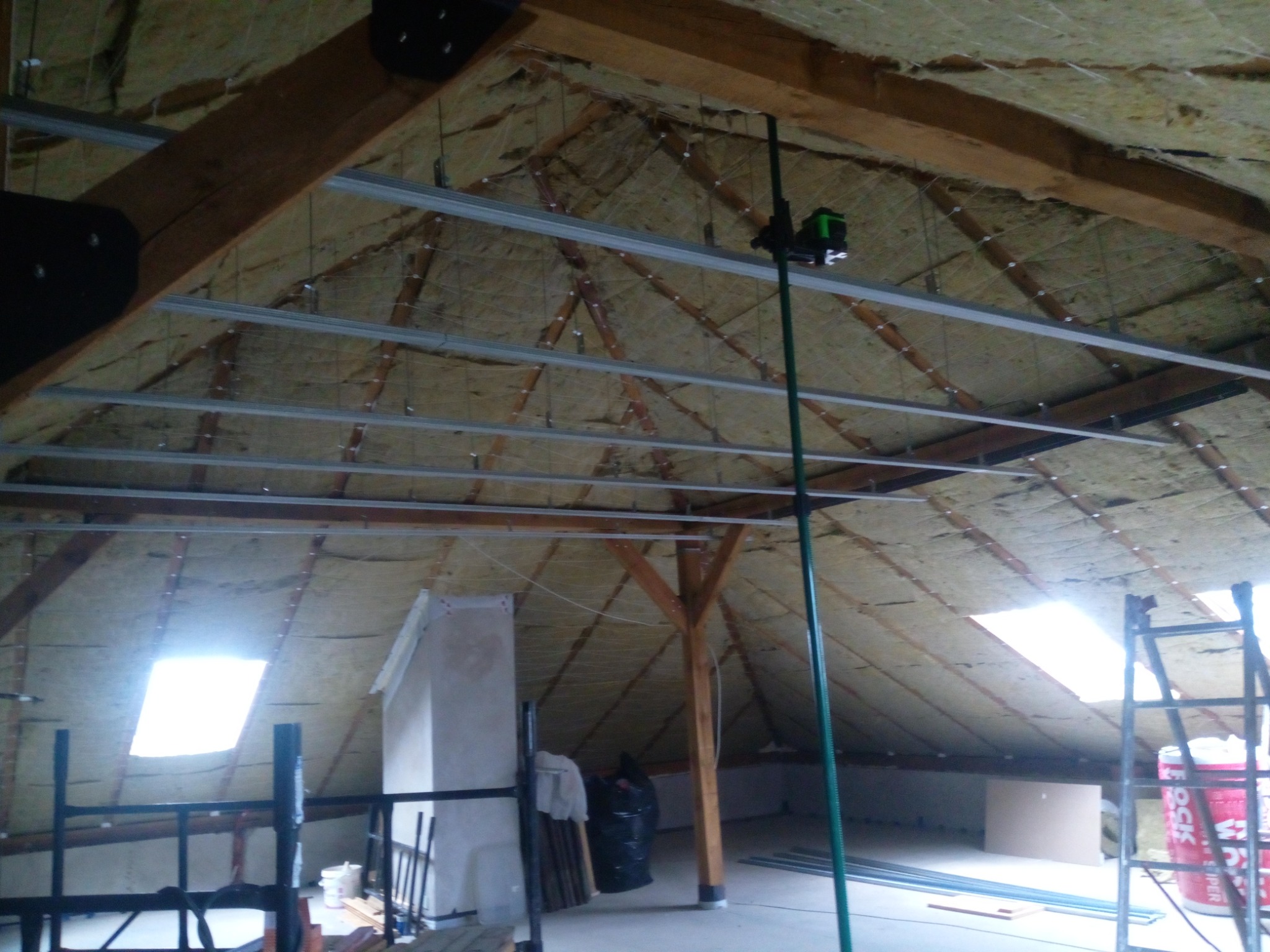 Poddasze w trakcie adaptacji: widoczne ocieplenie, metalowe profile sufitowe i laser krzyżowy na statywie, przygotowane do montażu okładziny.