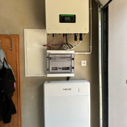Systemy Oze - Biały magazyn energii Sofar Solar zainstalowany w garażu, z podłączonym inwerterem i skrzynką bezpiecznikową na ścianie.