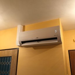 Systemy Oze - Klimatyzator LG Dual Inverter zamontowany na żółtej ścianie w pomieszczeniu, widoczny wyświetlacz z temperaturą 30 stopni Celsjusza.