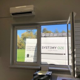 Systemy Oze - Wnętrze biura z widokiem przez okno na zaparkowany samochód dostawczy firmy instalującej odnawialne źródła energii, na ścianie klimatyzator LG.