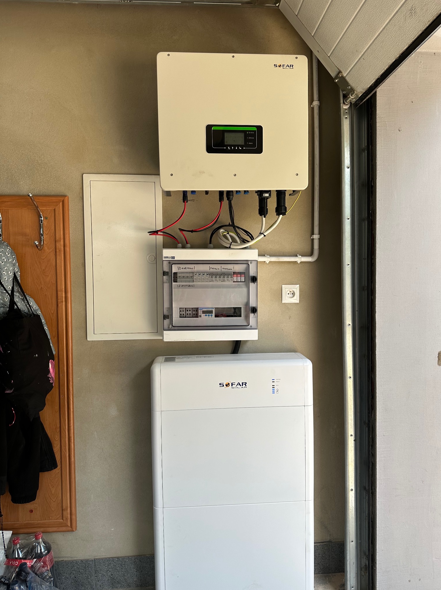 Biały magazyn energii Sofar Solar zainstalowany w garażu, z podłączonym inwerterem i skrzynką bezpiecznikową na ścianie.