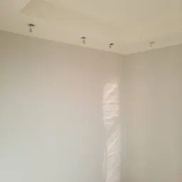 Pomalowane na szaro wnętrze pokoju z zamontowanymi czterema punktowymi lampami sufitowymi i marmurową podłogą.