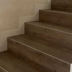 Schody wykończone panelami imitującymi drewno z białymi listwami przypodłogowymi, widok z dołu ukazujący fakturę paneli i precyzję wykonania.