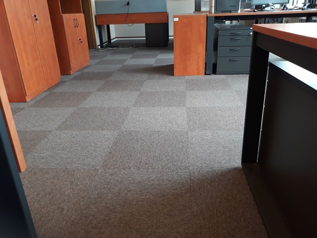 Biuro z podłogą pokrytą wykładziną w szachownicę, widoczne szafy i biurka w tle.