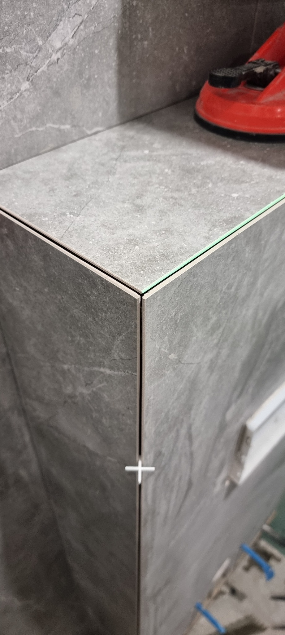 Szare płytki imitujące kamień, ułożone pod kątem, z widocznymi krzyżykami dystansowymi i przyssawką do płytek na górnej powierzchni, ukazujące precyzję wykonania.