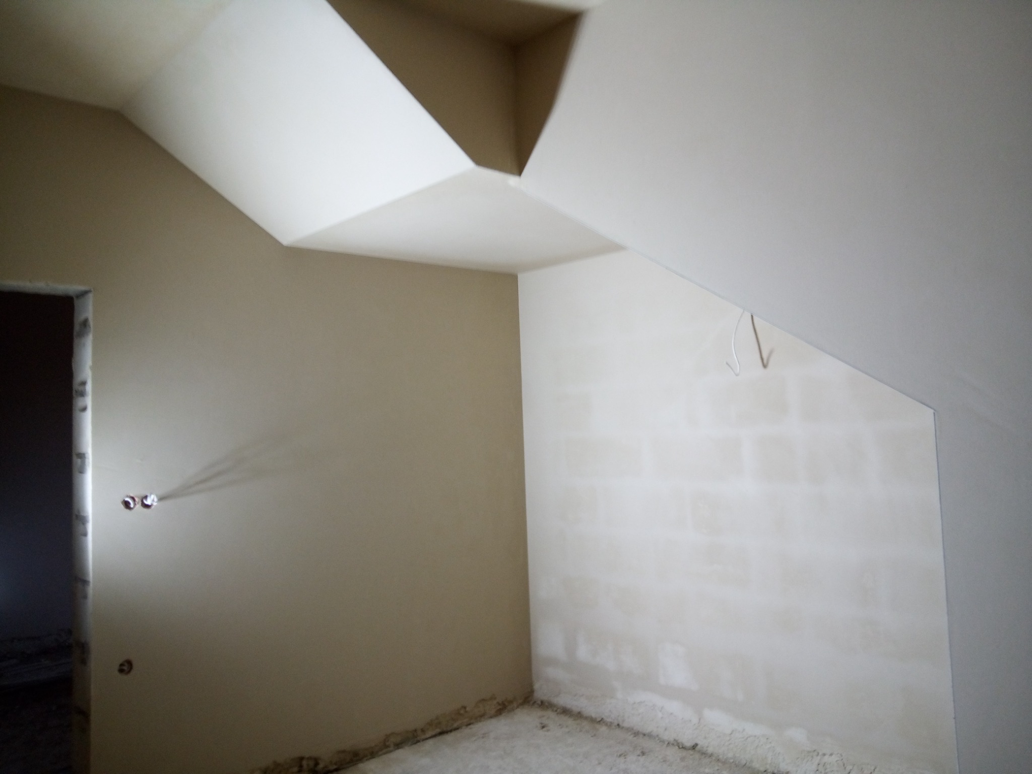 Pokój na poddaszu po nałożeniu warstwy szpachli, widoczne gniazdka elektryczne i niedoskonałości na ścianie z cegieł.
