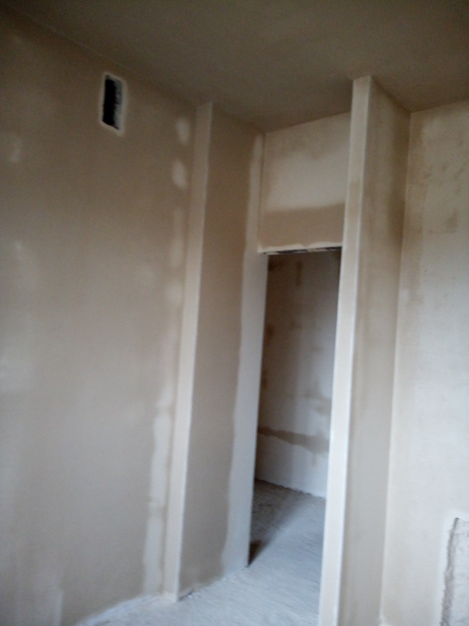 Ściana w trakcie prac wykończeniowych, widoczne nierówności i ślady po szpachlowaniu, przygotowana do dalszej obróbki, zarys otworu drzwiowego z wyraźnie zaznaczonymi ościeżnicami.