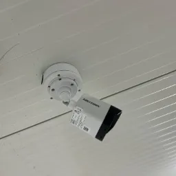 Kamera monitoringu Hikvision zamontowana na białym, panelowym suficie, widoczne drobne zabrudzenia i zarysowania na powierzchni.