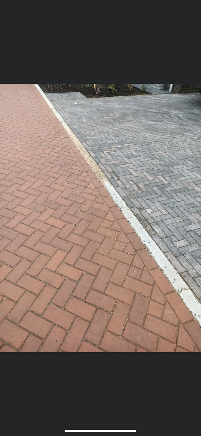 Dwa rodzaje kostki ułożone w jodełkę: czerwona i szara, oddzielone betonowym obrzeżem, z widocznymi drobnymi kamyczkami w spoinach.