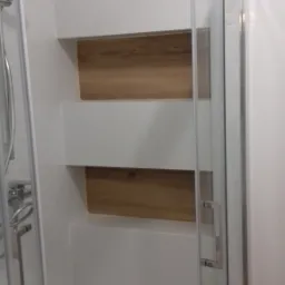 Nowoczesna kabina prysznicowa z wnękami wykończonymi drewnopodobnymi płytkami, chromowana armatura, białe płytki na ścianach.