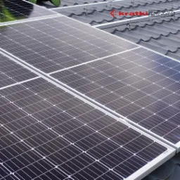 Panele słoneczne na ciemnoszarym dachu z dachówki ceramicznej, widoczny system montażowy i logo Kratki Energy.