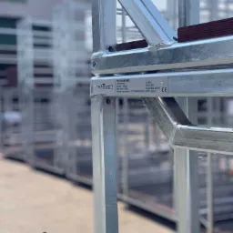 Szczegółowe ujęcie metalowej ramy kontenera paletowego, widoczne spawy i tabliczka znamionowa z danymi technicznymi, w tle inne kontenery.