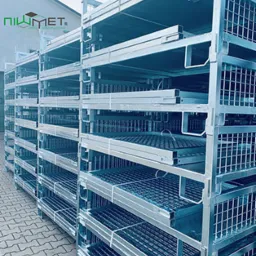 Stos metalowych, ocynkowanych palet siatkowych z logo firmy Niwmet, ustawionych na zewnątrz budynku.