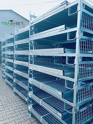Stos metalowych, ocynkowanych palet siatkowych z logo firmy Niwmet, ustawionych na zewnątrz budynku.