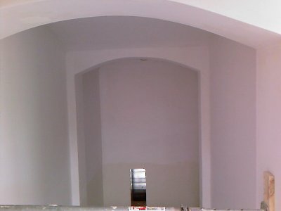 Świeżo otynkowane, białe ściany z łukowatymi przejściami wewnątrz pomieszczenia, widoczne ślady po rusztowaniu.