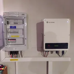 Rozdzielnica PV-AC i PV-DC firmy KENO z otwartymi drzwiczkami, obok biały inwerter fotowoltaiczny GoodWe na białej półce przy ścianie.